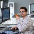 Junger Softwareentwickler mit Kaffeetasse an einem Arbeitsplatz mit mehreren Monitoren voller Code