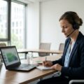 Beschäftigte nimmt mit Headset und Notizbuch am Laptop an einer digitalen Schulung teil